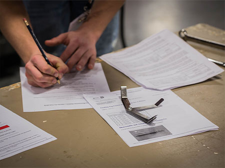 person holding pencil and taking test with papers laid out on desk